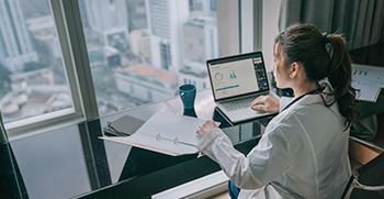 A woman looking at her laptop and her written notes at her desk